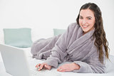 Relaxed brunette in bathrobe using laptop in bed