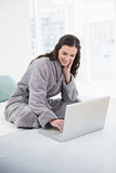 Casual brunette in bathrobe using laptop in bed