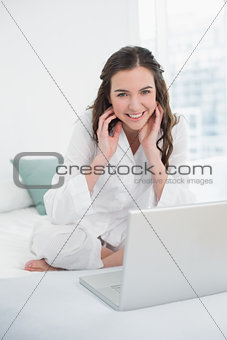 Smiling casual brunette with laptop sitting in bed