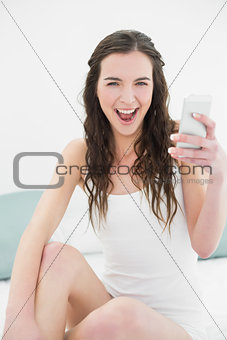Cheerful woman with mobile phone in bed