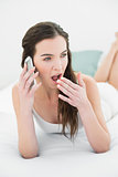 Sleepy woman yawning while using mobile phone in bed