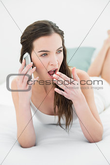Sleepy woman yawning while using mobile phone in bed