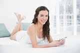 Smiling young woman with mobile phone in bed