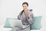Woman in bathrobe doing online shopping in bed