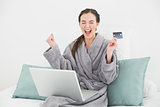 Excited woman in bathrobe doing online shopping