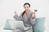 Excited woman in bathrobe doing online shopping in bed
