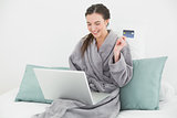 Casual woman in bathrobe doing online shopping in bed