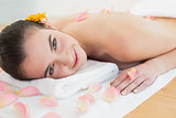 Beautiful woman resting on towel with petals at beauty spa