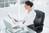 Businesswoman reading newspaper and using laptop in office