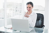 Businesswoman drinking coffee while using laptop at desk