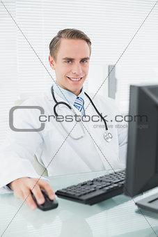 Confident smiling male doctor with computer at medical office