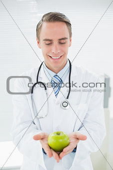 Smiling male doctor holding a green apple