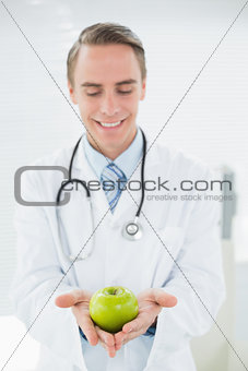 Smiling male doctor holding a green apple
