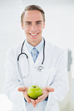 Portrait of a smiling male doctor holding a green apple