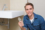 Smiling plumber with wrench by sink in bathroom