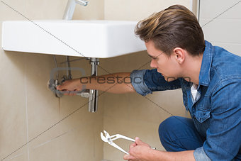Handsome plumber with wrench by sink in bathroom