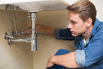Handsome plumber repairing washbasin drain in bathroom