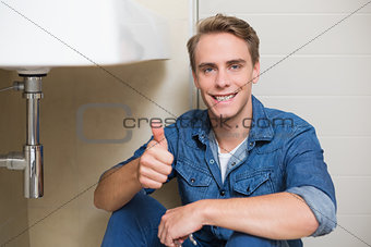 Handsome plumber gesturing thumbs up besides washbasin