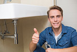 Handsome plumber gesturing thumbs up besides washbasin