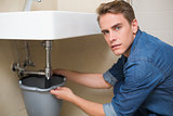 Handsome plumber repairing the drain of sink