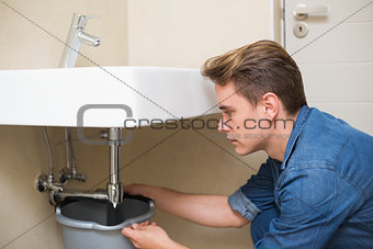 Handsome plumber repairing the drain of sink