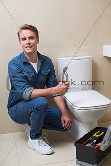 Handsome plumber with toolbox doing toilet reparation