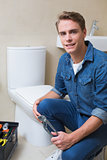 Handsome plumber with toolbox doing toilet reparation