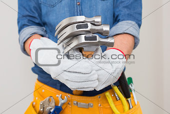 Mid section of handyman holding hammers with toolbelt around waist
