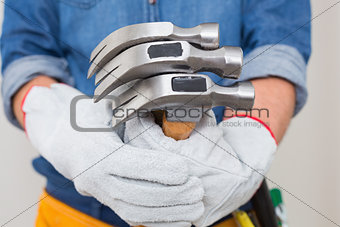 Mid section of a handyman holding hammers with toolbelt around waist