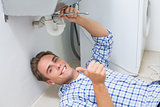 Plumber repairing washbasin drain while gesturing thumbs up