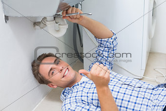 Plumber repairing washbasin drain while gesturing thumbs up