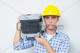 Serious handyman in yellow hard hat carrying toolbox
