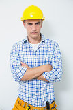 Serious handyman in yellow hard hat with arms crossed