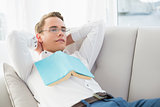 Relaxed thoughtful man with book lying on sofa