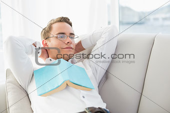 Relaxed thoughtful young man with book lying on sofa