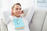 Relaxed thoughtful young man with book lying on sofa