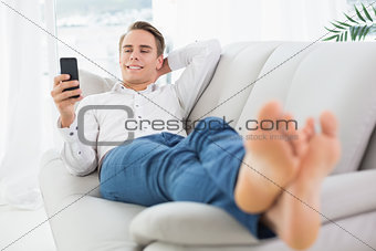 Relaxed man lying on sofa and text messaging