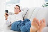 Relaxed young man lying on sofa and text messaging