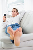 Relaxed young man lying on sofa and text messaging