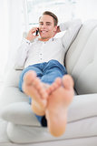Relaxed young man using cellphone while lying on sofa