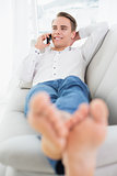 Relaxed young man using cellphone while lying on sofa