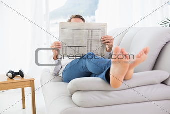 Relaxed man reading newspaper on sofa