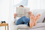 Full length of a relaxed man reading newspaper on sofa