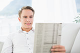 Smiling relaxed man reading newspaper on sofa