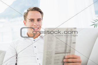 Portrait of a smiling man reading newspaper on sofa