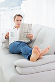 Relaxed man with coffee cup while reading newspaper on sofa