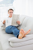 Relaxed man with coffee cup while reading newspaper on sofa