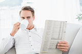 Relaxed man drinking coffee while reading newspaper on sofa