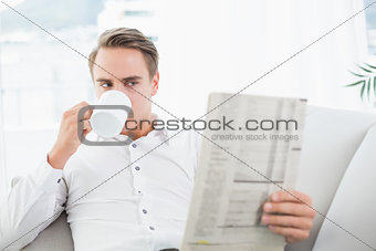 Relaxed man drinking coffee while reading newspaper on sofa