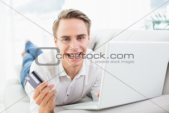 Cheerful man doing online shopping on sofa at home